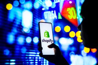 Editorial use only. September 13, 2022, Brazil. In this photo illustration, a silhouetted woman holds a smartphone with the Shopify logo displayed on the screen