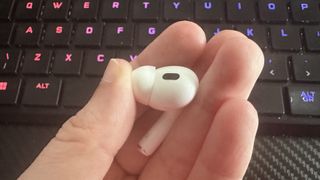 Someone holding Apple AirPods Pro in their hands next to a keyboard.