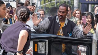 Axel Foley surrenders to two police officers outside an overturned vehicle as a crowd films him on their phones.